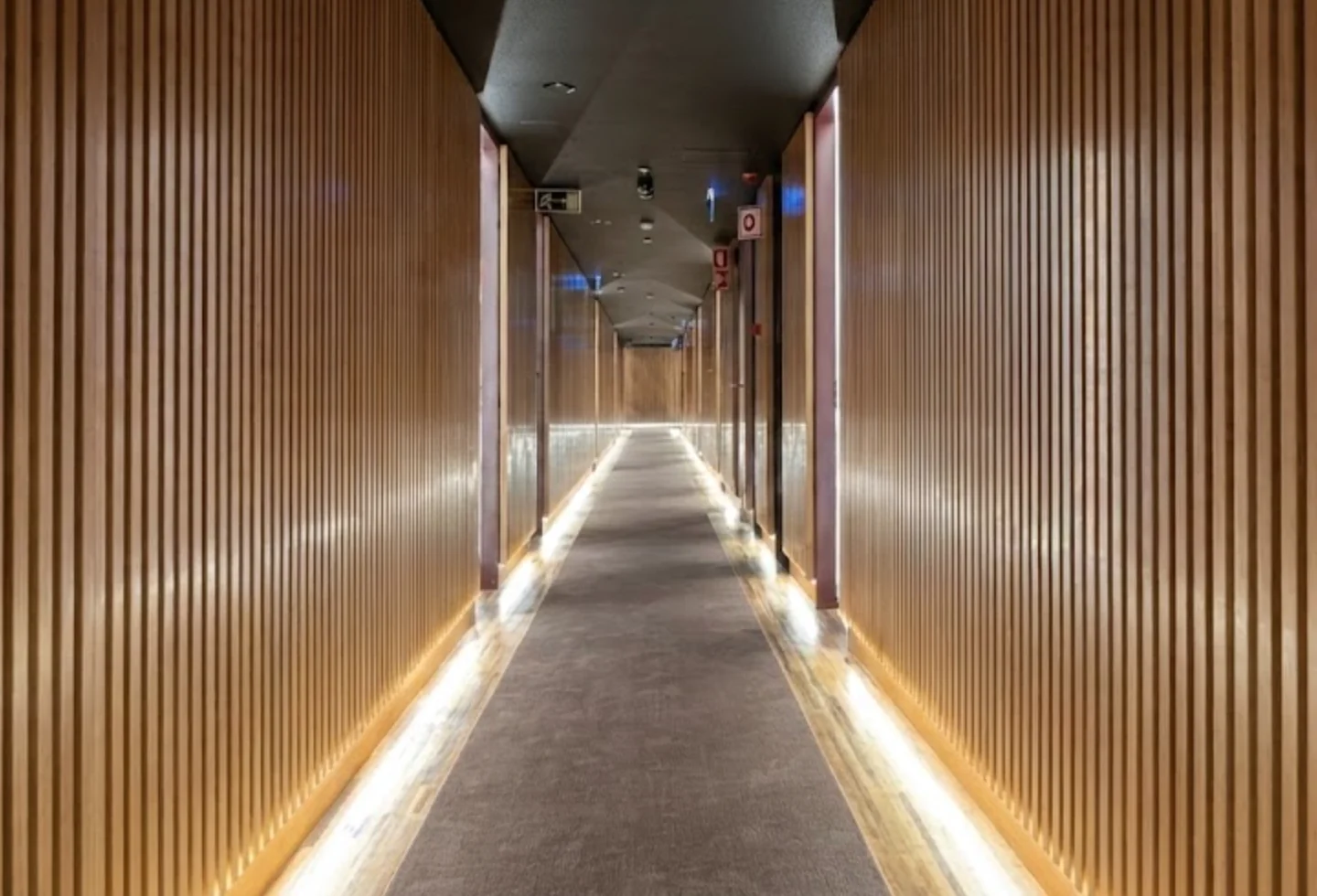 Hotel hallway showcasing the fusion of warm wood paneling and modern LED lighting
